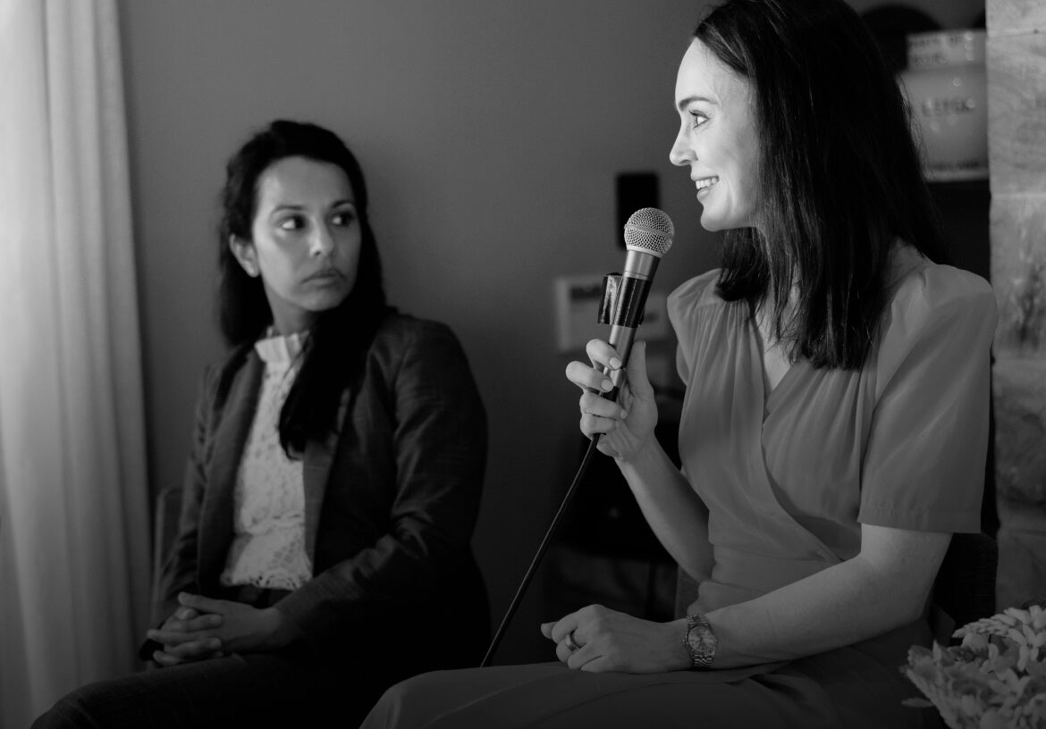 Woman holding a microphone speaking to another woman in a room.