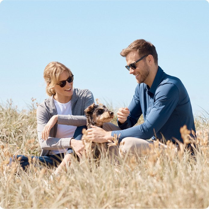 Two people sitting in a field with a dog on a clear day
